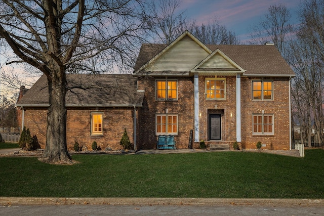 neoclassical home featuring roof with shingles, brick siding, a chimney, and a lawn