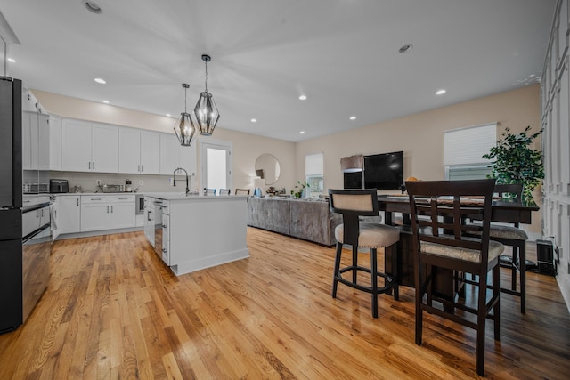 kitchen featuring light wood finished floors, white cabinets, open floor plan, a kitchen island with sink, and light countertops