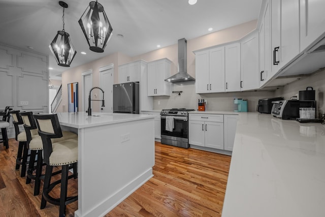 kitchen with stainless steel appliances, light wood-type flooring, an island with sink, and wall chimney exhaust hood