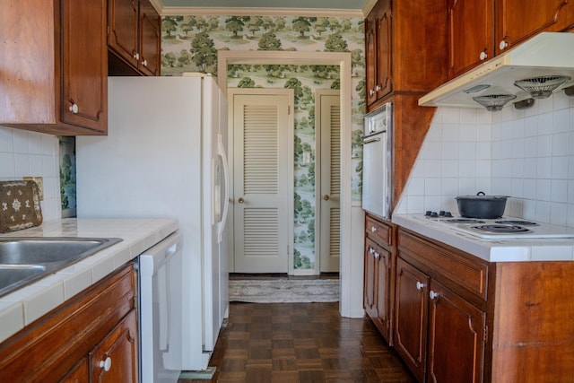 kitchen featuring tile counters, decorative backsplash, white appliances, under cabinet range hood, and wallpapered walls