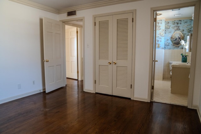 unfurnished bedroom featuring dark wood-type flooring, a closet, visible vents, and crown molding