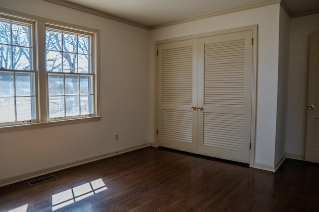 unfurnished bedroom featuring visible vents, baseboards, ornamental molding, a closet, and dark wood finished floors