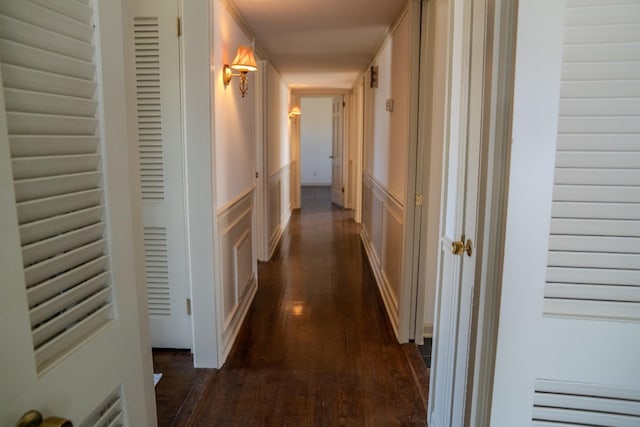 hall featuring a wainscoted wall, dark wood finished floors, and a decorative wall