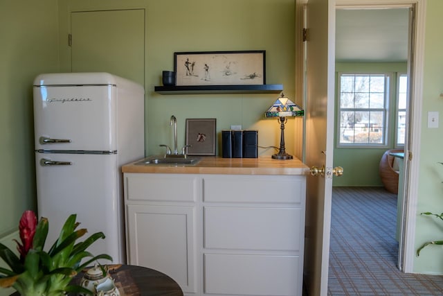 kitchen featuring wooden counters, freestanding refrigerator, carpet flooring, a sink, and white cabinetry