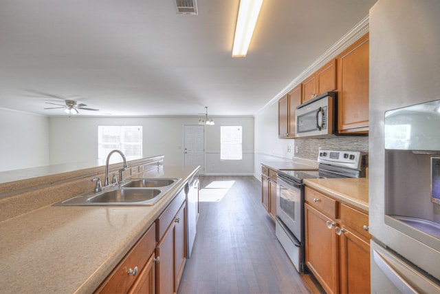 kitchen with a sink, appliances with stainless steel finishes, brown cabinetry, dark wood finished floors, and crown molding