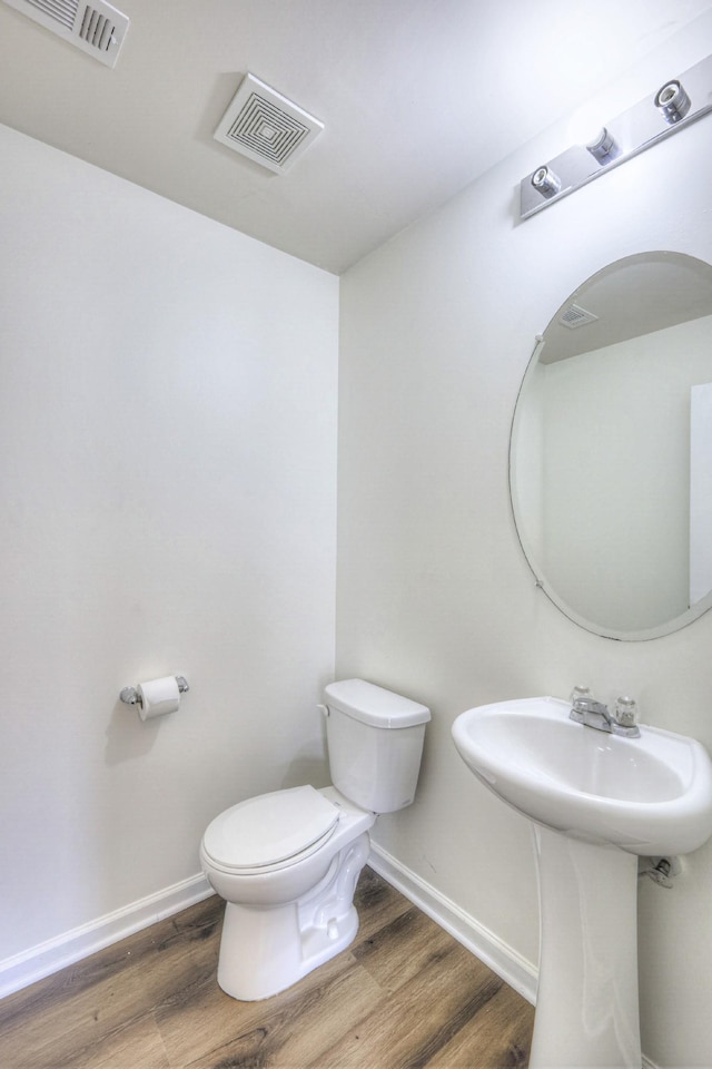 half bath featuring toilet, wood finished floors, visible vents, and baseboards