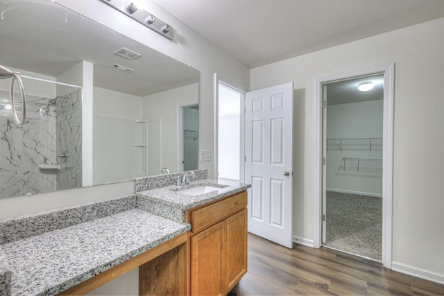 bathroom with wood finished floors, visible vents, vanity, a marble finish shower, and a walk in closet