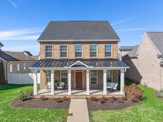 view of front of house featuring a standing seam roof, fence, metal roof, and brick siding