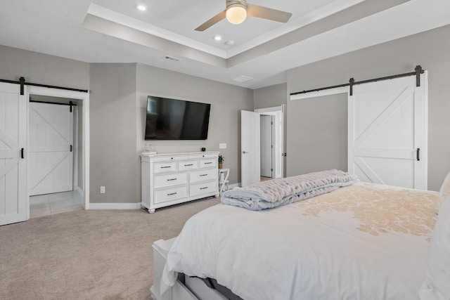 bedroom with a tray ceiling, a barn door, visible vents, and light colored carpet