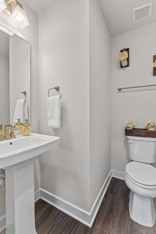 bathroom with visible vents, toilet, a sink, wood finished floors, and baseboards