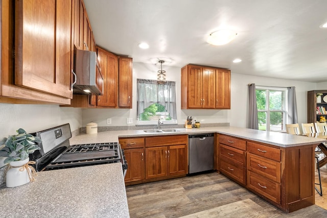 kitchen featuring light countertops, appliances with stainless steel finishes, brown cabinetry, a sink, and a peninsula