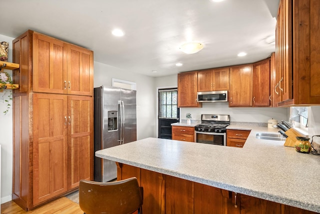 kitchen featuring stainless steel appliances, a peninsula, a sink, light countertops, and brown cabinets