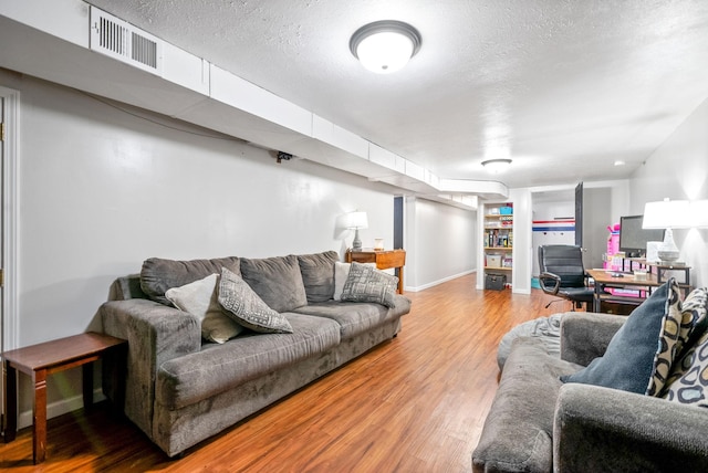 living room with built in features, visible vents, a textured ceiling, wood finished floors, and baseboards