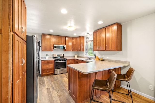 kitchen featuring light wood finished floors, a peninsula, appliances with stainless steel finishes, and brown cabinetry