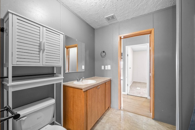 bathroom with toilet, visible vents, a textured ceiling, and vanity