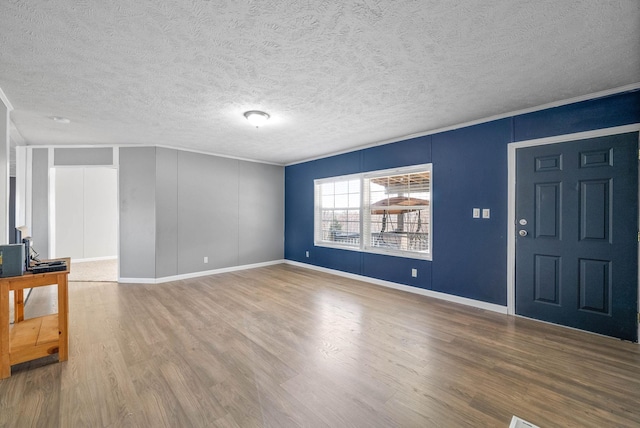 unfurnished living room featuring crown molding, a textured ceiling, baseboards, and wood finished floors