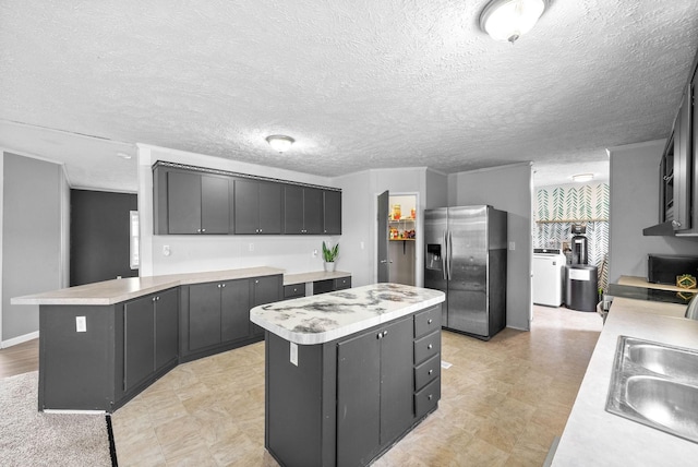 kitchen featuring a sink, stainless steel fridge with ice dispenser, light countertops, a center island, and washer and clothes dryer