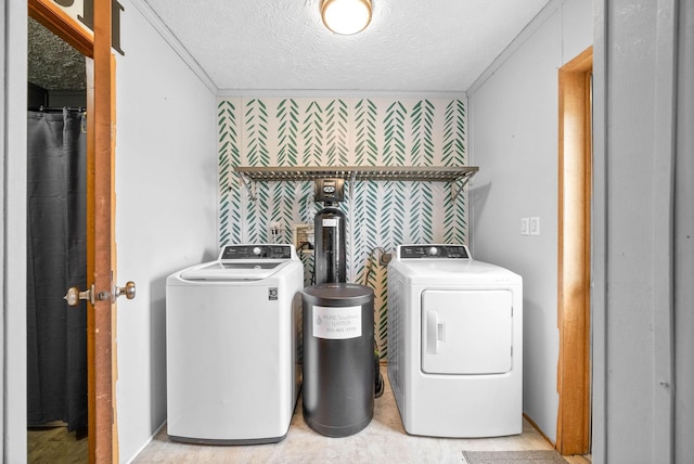 laundry area with a textured ceiling, an accent wall, separate washer and dryer, and wallpapered walls