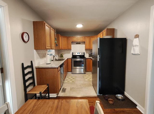 kitchen featuring light countertops, backsplash, appliances with stainless steel finishes, a sink, and under cabinet range hood