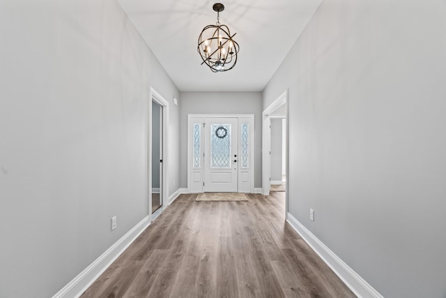 doorway to outside with a notable chandelier, baseboards, and wood finished floors