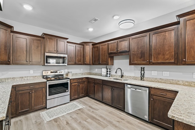 kitchen with stainless steel appliances, light wood-style floors, a sink, dark brown cabinetry, and light stone countertops