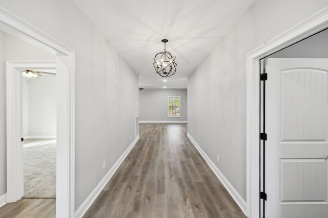 corridor with a notable chandelier, baseboards, and wood finished floors