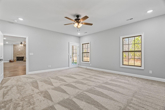 empty room featuring a brick fireplace, plenty of natural light, visible vents, and carpet flooring