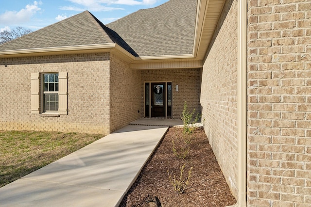 entrance to property featuring brick siding and roof with shingles