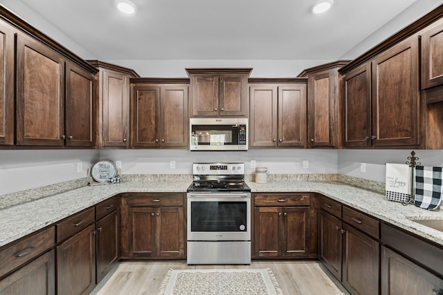 kitchen featuring stainless steel appliances, dark brown cabinetry, light wood finished floors, and light stone countertops