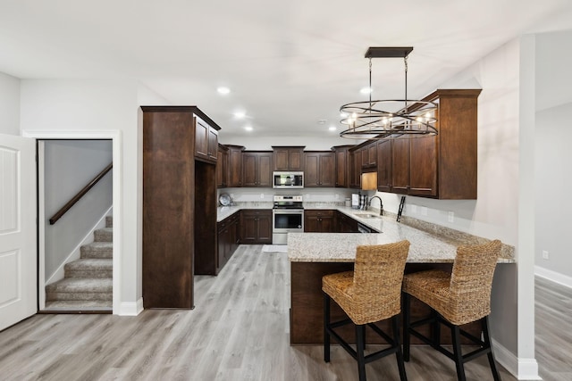 kitchen featuring stainless steel appliances, a peninsula, a sink, dark brown cabinets, and light stone countertops