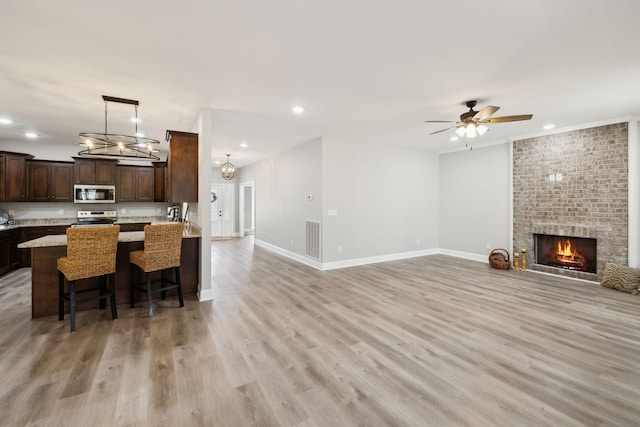 kitchen featuring dark brown cabinetry, light wood finished floors, visible vents, appliances with stainless steel finishes, and open floor plan