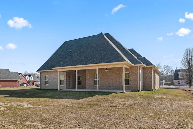 back of house featuring brick siding, a shingled roof, a lawn, a ceiling fan, and a patio area