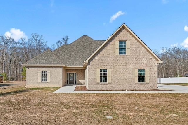 back of property with a yard, brick siding, roof with shingles, and fence