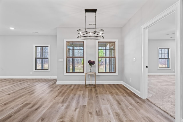 unfurnished dining area with a chandelier, wood finished floors, and baseboards