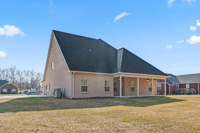 rear view of house featuring brick siding, a lawn, a patio, and roof with shingles