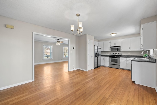 kitchen featuring appliances with stainless steel finishes, dark countertops, a sink, and light wood-style floors