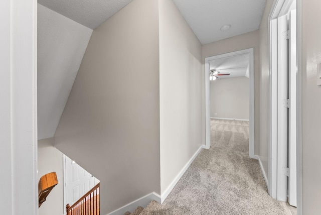 hallway with carpet floors, vaulted ceiling, a textured ceiling, and baseboards