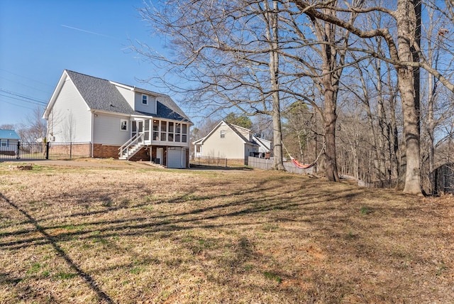 back of house featuring a garage, a lawn, fence, and a sunroom