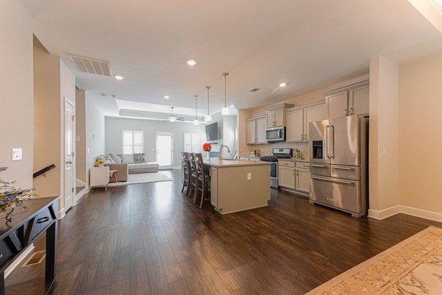 kitchen with dark wood-style floors, stainless steel appliances, visible vents, open floor plan, and a kitchen breakfast bar