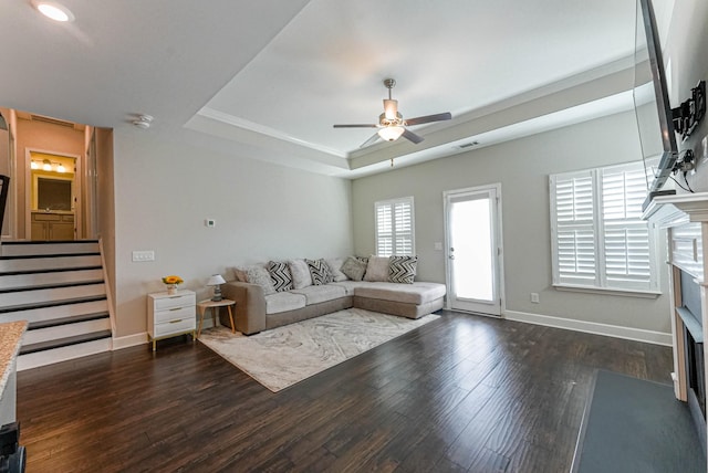 unfurnished living room featuring a fireplace with flush hearth, a tray ceiling, stairs, and wood finished floors