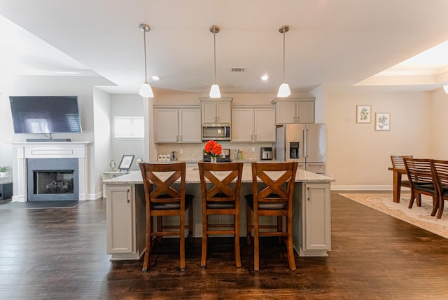 kitchen featuring stainless steel appliances, tasteful backsplash, dark wood finished floors, and a center island with sink