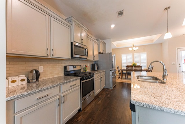 kitchen with stainless steel appliances, a sink, dark wood finished floors, backsplash, and a raised ceiling