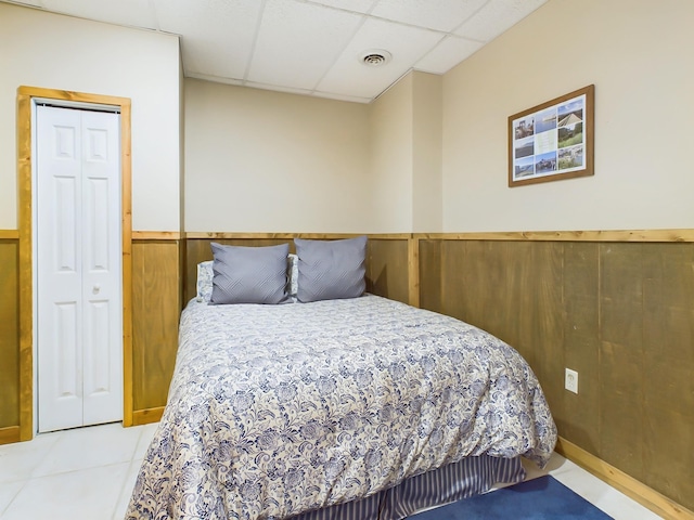 tiled bedroom featuring a wainscoted wall, a paneled ceiling, visible vents, and wooden walls