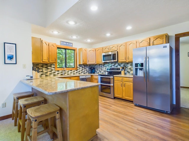 kitchen featuring a peninsula, a sink, appliances with stainless steel finishes, light wood finished floors, and tasteful backsplash