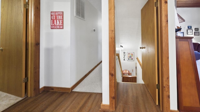 hall with baseboards, visible vents, wood finished floors, and an upstairs landing