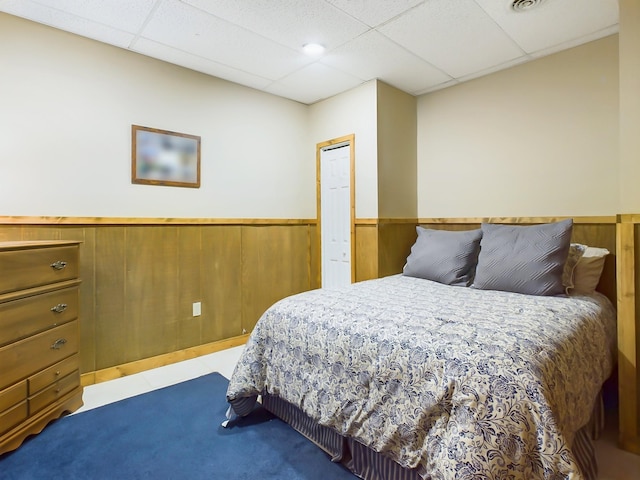 bedroom with visible vents, a wainscoted wall, wooden walls, and a drop ceiling