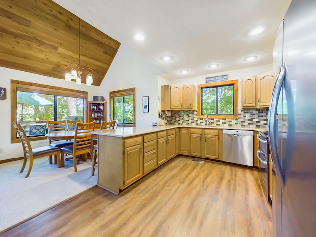 kitchen with appliances with stainless steel finishes, a peninsula, vaulted ceiling, light countertops, and a healthy amount of sunlight