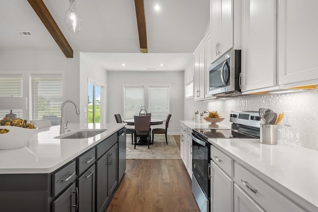 kitchen featuring light countertops, backsplash, appliances with stainless steel finishes, a sink, and beamed ceiling