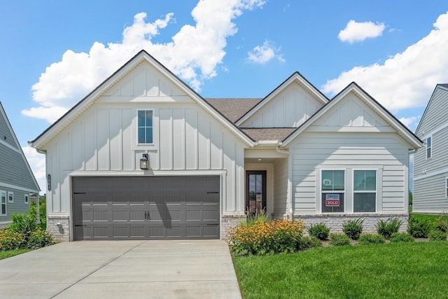 view of front of property with concrete driveway, stone siding, an attached garage, board and batten siding, and a front yard