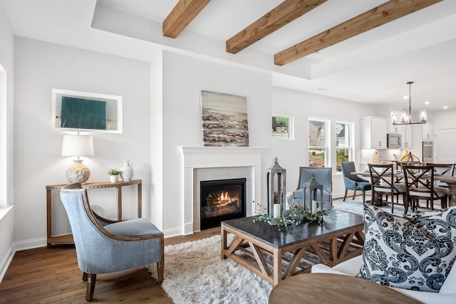 living room featuring a tile fireplace, wood finished floors, baseboards, beam ceiling, and an inviting chandelier